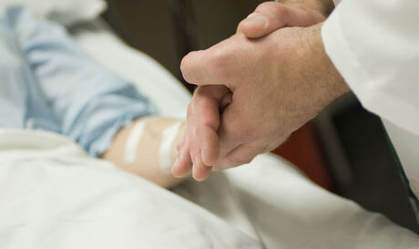Læge holder sengeliggende patients hånd